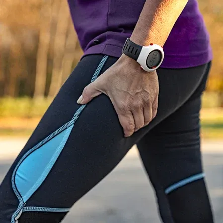 A person wearing athletic clothing and a smartwatch is holding the upper thigh, indicating possible muscle strain or sciatic pain.