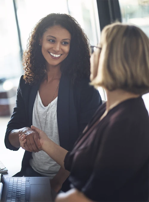 Two people are engaged in a handshake in a bright indoor setting, symbolizing agreement or partnership.